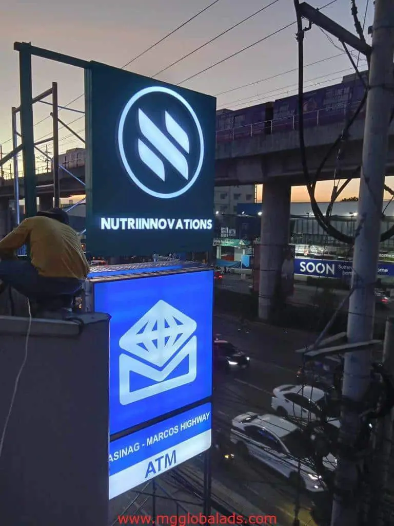 Illuminated LED signage for NUTRIINNOVATIONS and ATM in Makati, city street at dusk with cars and trains, by M&G Global Ads.