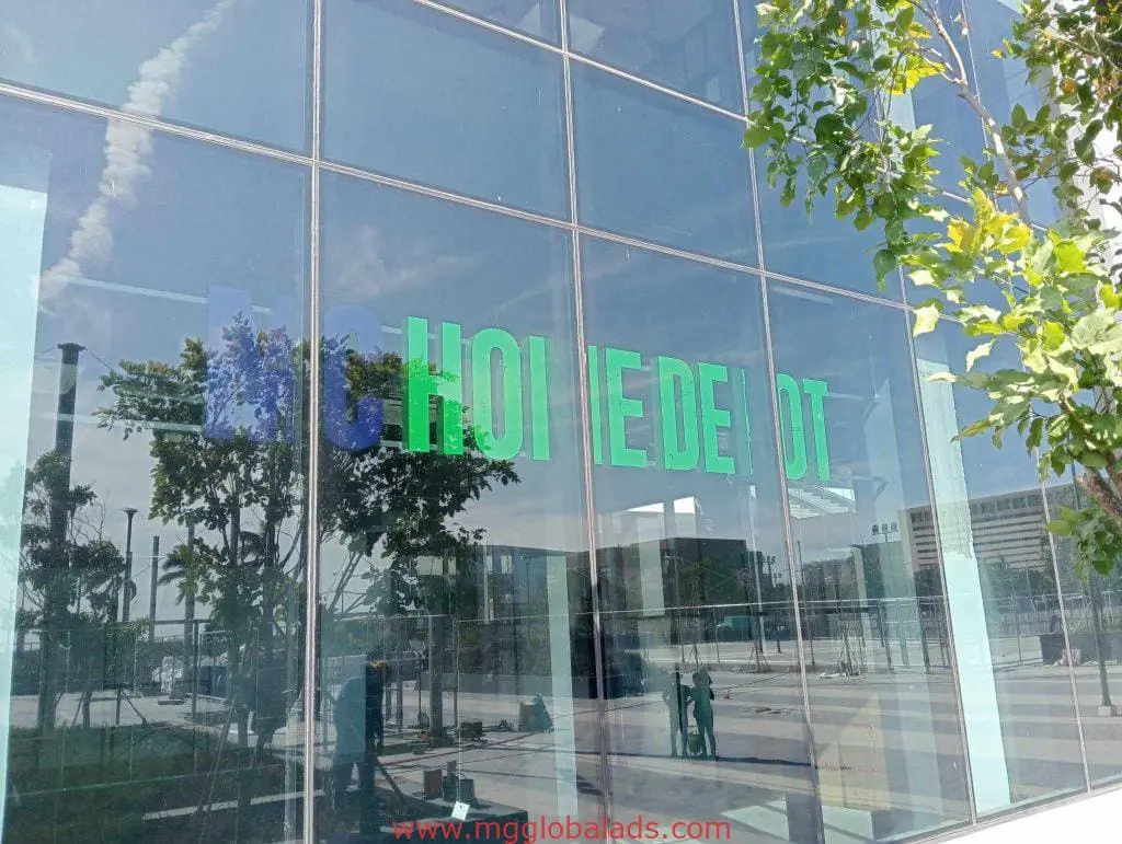 Metallic HOME DEPOT signage on a glass facade in Makati, reflecting trees and people outside by M&G Global Ads.