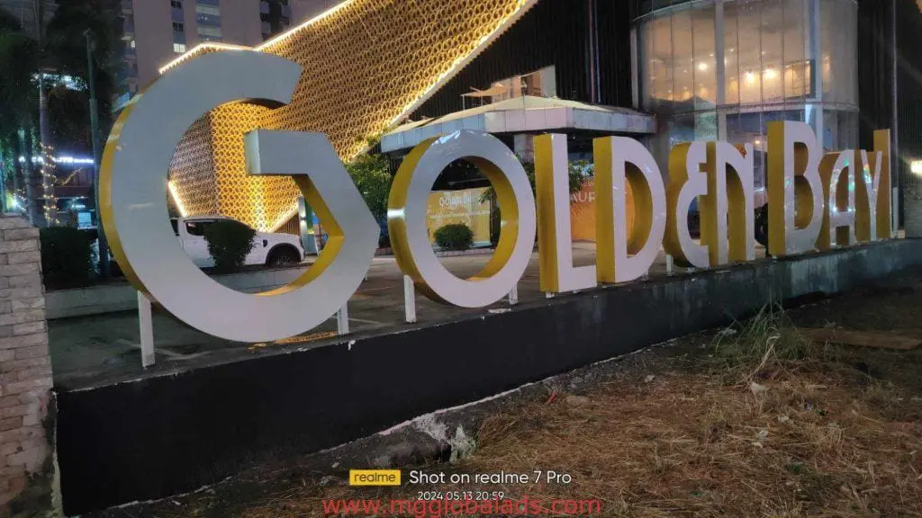 Illuminated acrylic GOLDEN BAY signage at modern building, Makati, with night lights and car. By M&G Global Ads.