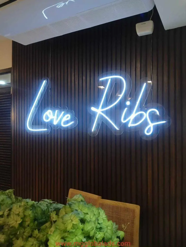 LED neon signage for Love Ribs on dark wood wall in Quezon City, with plants and woven chairs by M&G Global Ads.