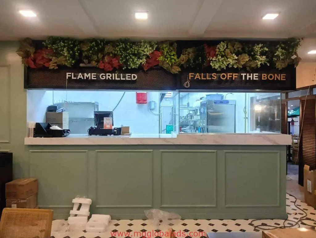 Bold indoor restaurant signage “FLAME GRILLED” & “FALLS OFF THE BONE” at marble counter in BGC by M&G Global Ads.