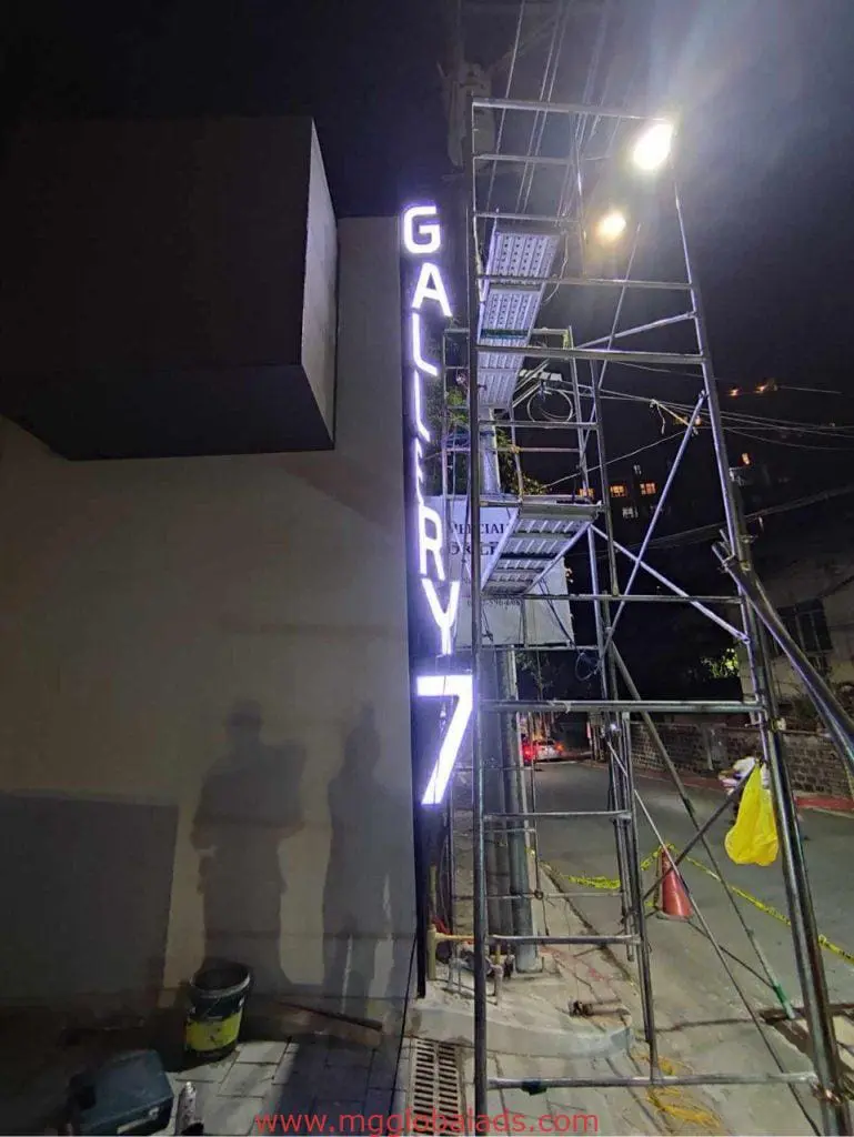 Vertical LED building signage for GALLERY 7 in Makati, next to scaffolding and a street at night by M&G Global Ads.