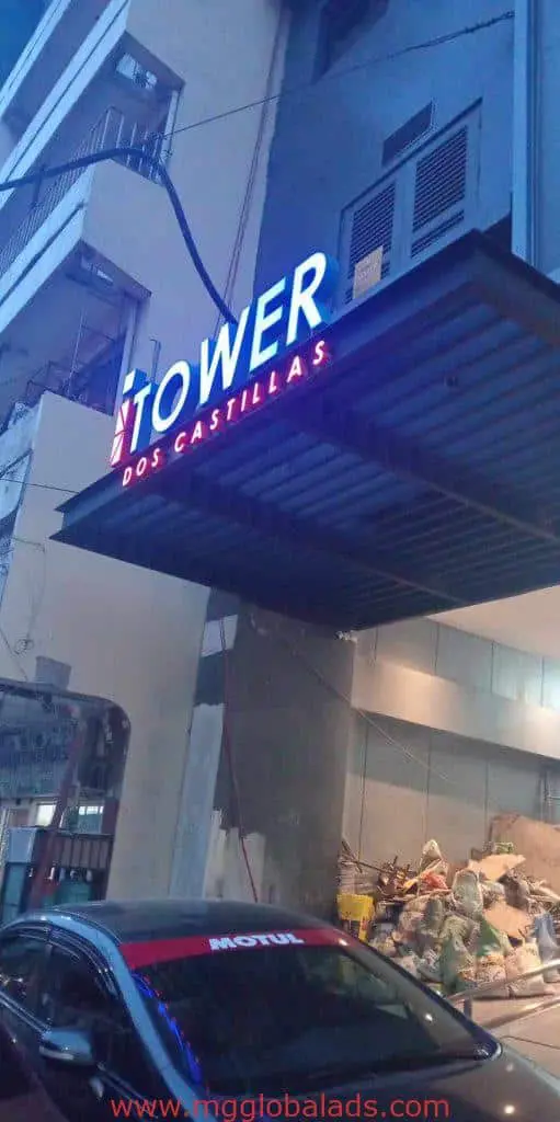 Outdoor metal signage TOWER DOS CASTILLAS in Quezon City, with debris and parked car, by M&G Global Ads.