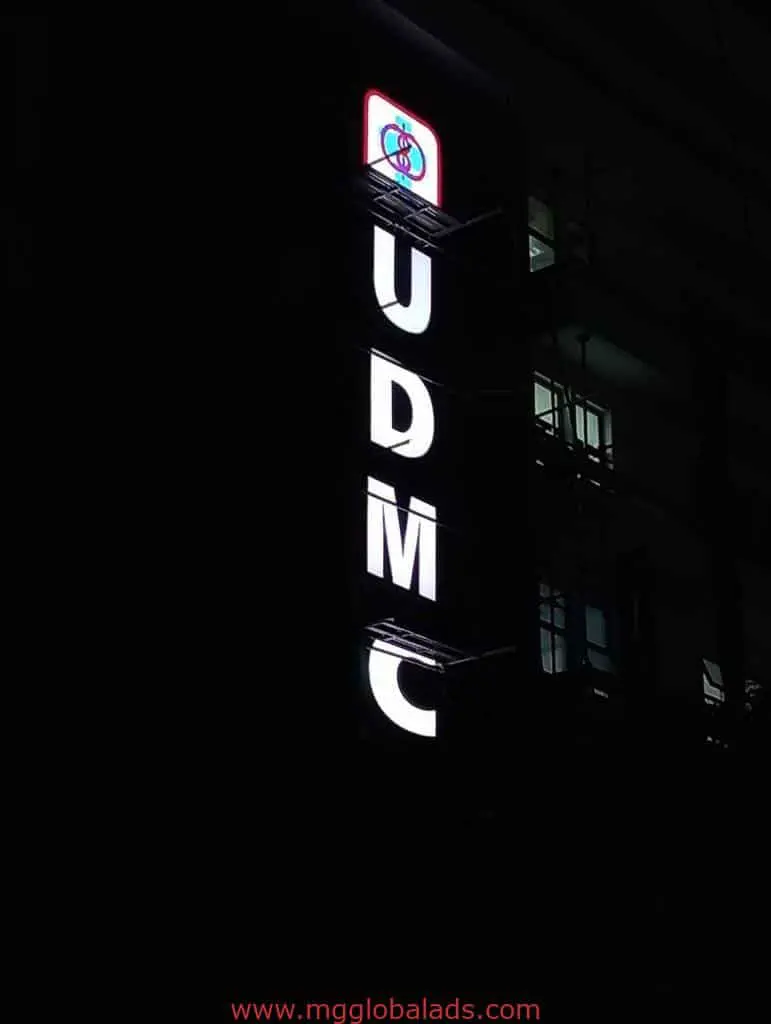 Acrylic LED signage for UDMC with circular logo, illuminated at night in Quezon City, by M&G Global Ads.