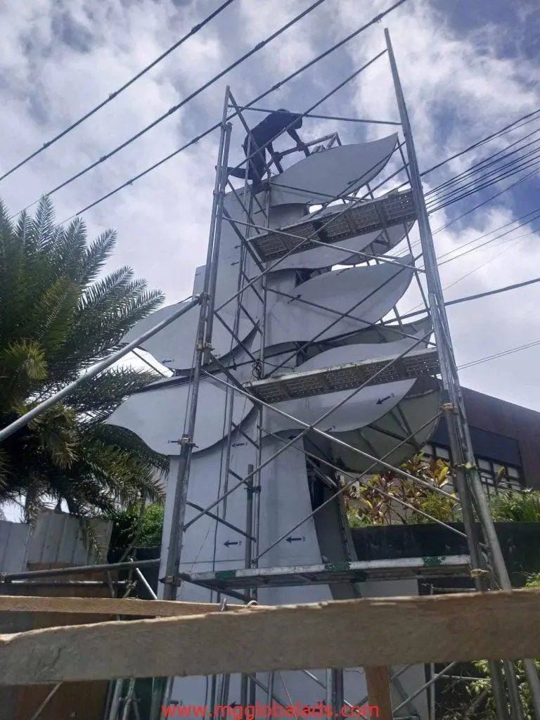 Worker on scaffolding installing satellite dishes beside outdoor LED signage in Quezon City by M&G Global Ads.