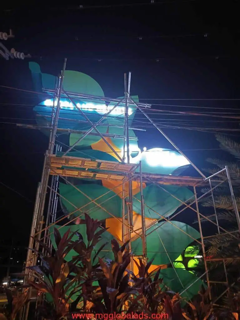 Custom metallic LED signage under construction at night in Ortigas, with scaffolding and plants, by M&G Global Ads.