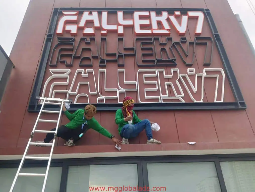 Metallic 3D building signage installation in Makati by M&G Global Ads, workers in green shirts adding bold neon-style sign.