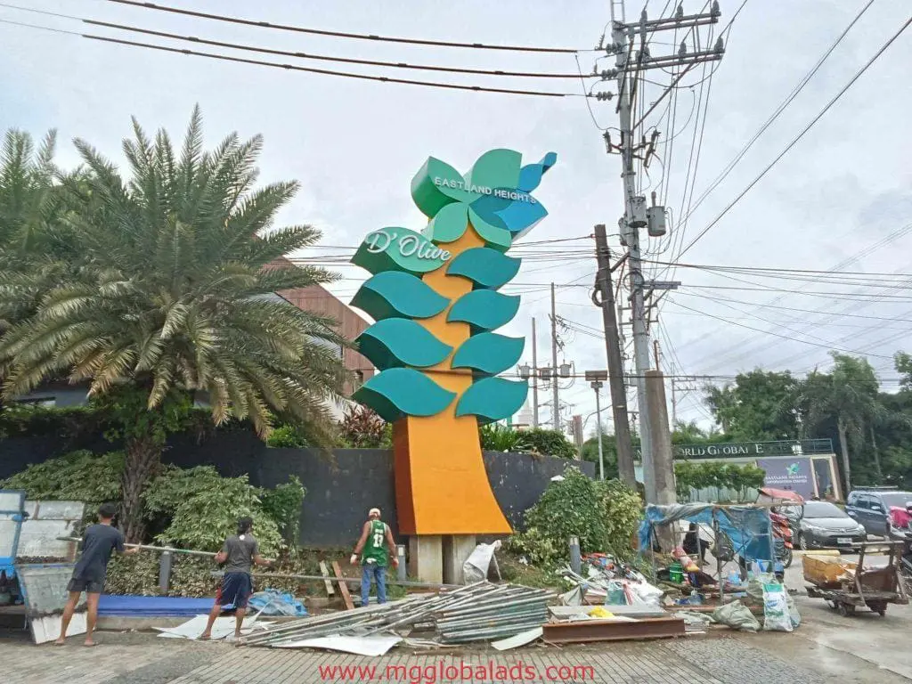 Eastland Heights D’Olive leaf-shaped outdoor signage installation in Quezon City, workers on-site, by M&G Global Ads.