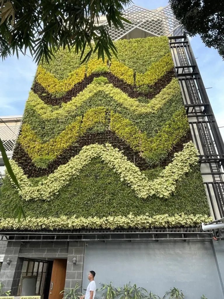 Metallic business signage on a building with vertical garden in Quezon City, person nearby, by M&G Global Ads.