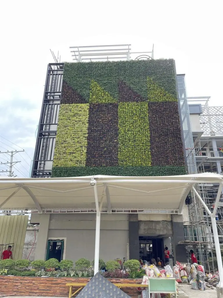 Metallic building signage on a lush vertical garden in Makati, with workers and plants at entrance, by M&G Global Ads.