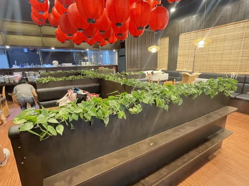 Restaurant with indoor acrylic signage, black booths, plants, red lanterns in Makati; person near booths. By M&G Global Ads.