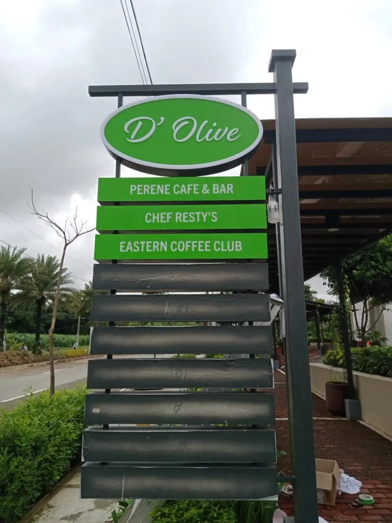 Outdoor pylon signage for DOlive featuring PERENE CAFE & BAR in Makati, with trees and a building, by M&G Global Ads.
