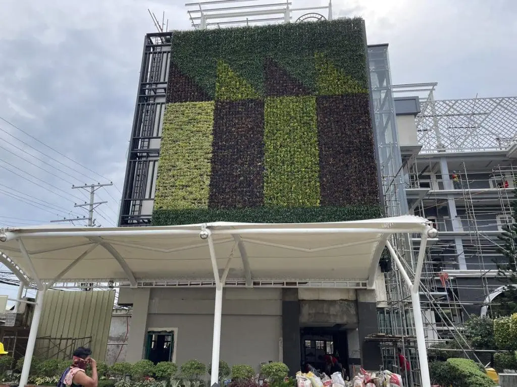 Outdoor business signage installation with vertical garden facade, scaffolding, and people in Makati by M&G Global Ads.
