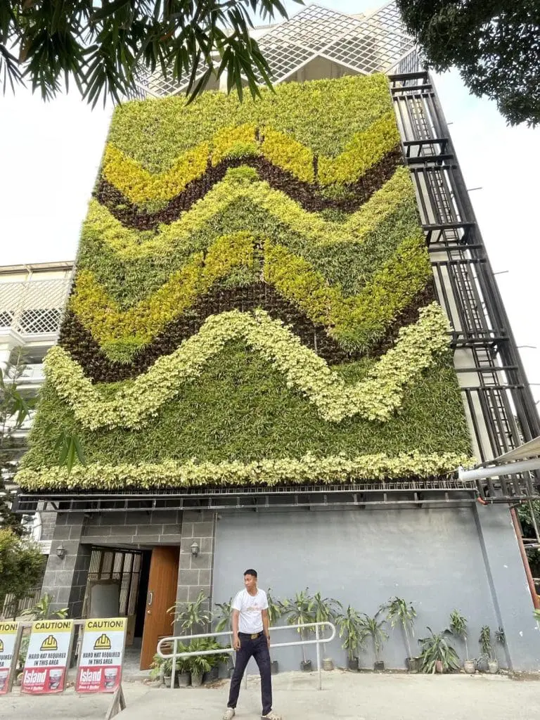 Building facade with Greenwall and Moss Wall. safety caution signage, and a man in Makati by M&G Global Ads.
