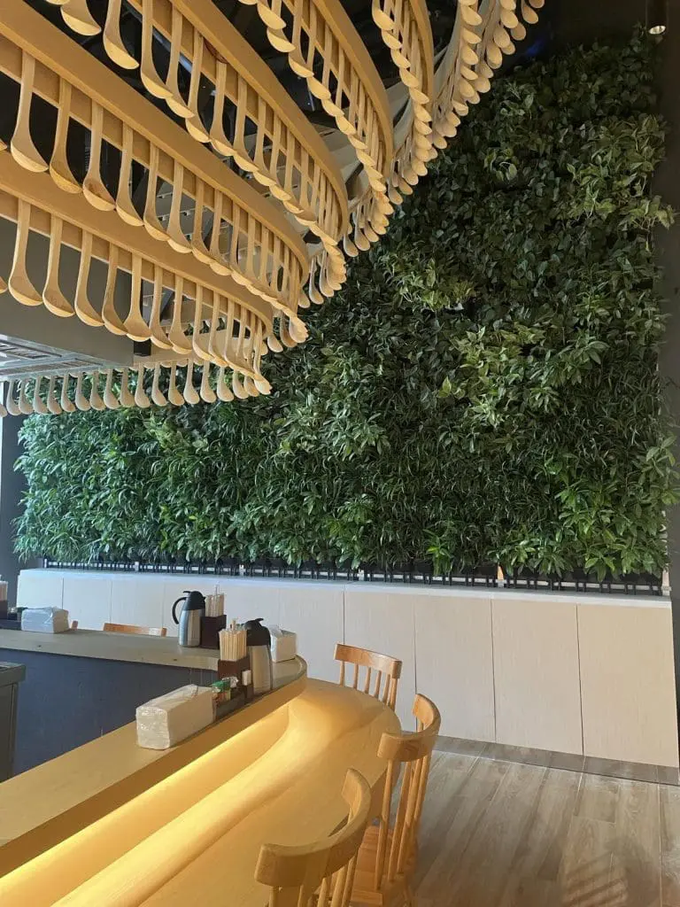 Modern restaurant with light wood furniture, curved ceiling, plant wall, and indoor wayfinding signage in BGC by M&G Global Ads.