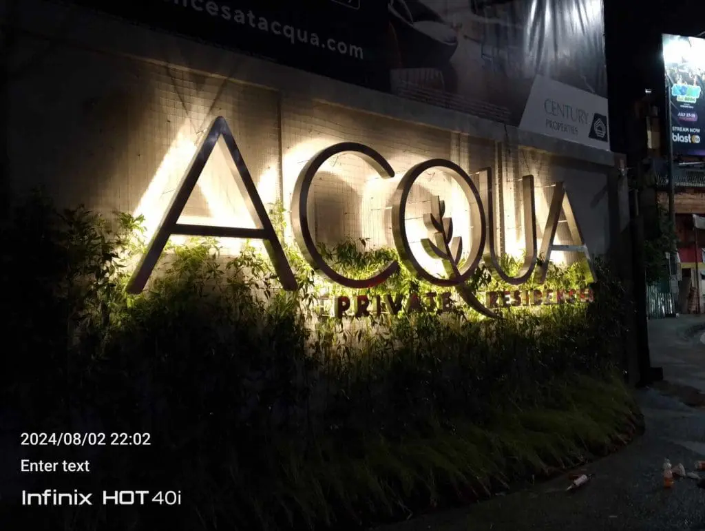 Illuminated metallic signage for ACQUA PRIVATE RESIDENCES at night in Makati, greenery visible, by M&G Global Ads.