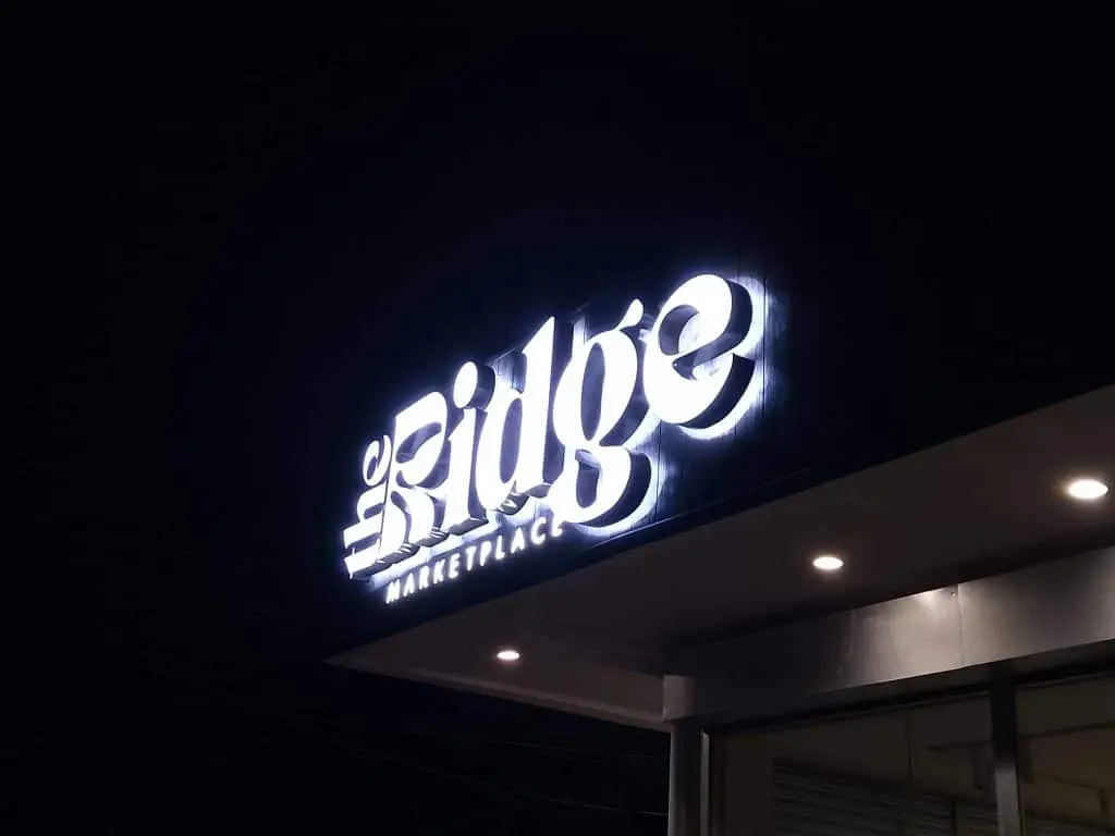 The Ridge Marketplace lighted outdoor signage at modern building entrance in BGC at night by M&G Global Ads.