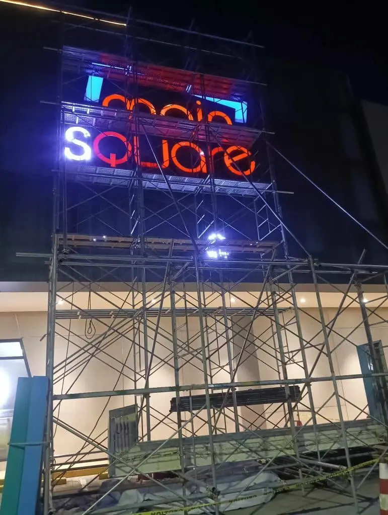 LED metallic signage for Moon Square in Ortigas, partially covered by scaffolding and tape at night, by M&G Global Ads.