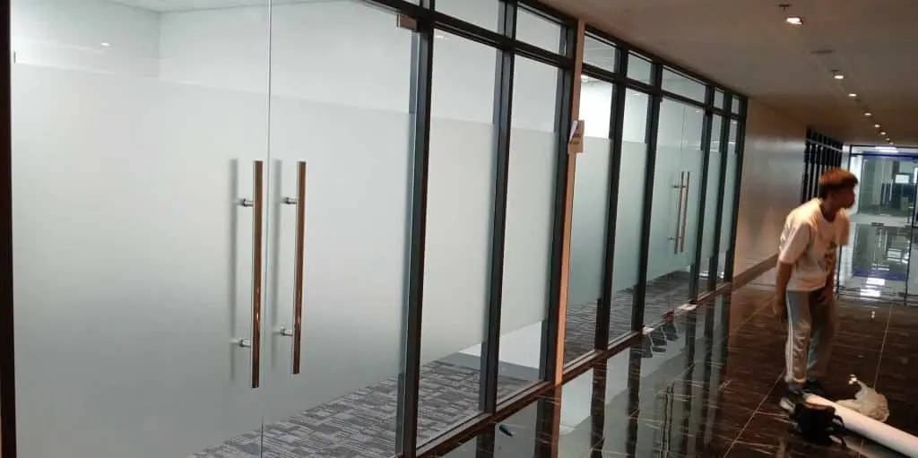 Acrylic office signage on glass doors in modern hallway, shiny black tile floor in Makati office building by M&G Global Ads.