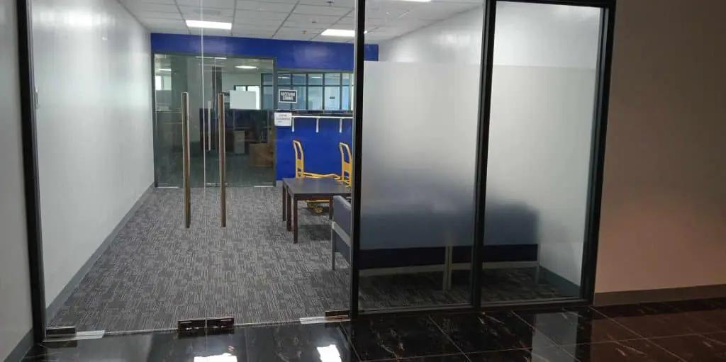 Office indoor acrylic signage in a modern Makati workspace with glass doors, blue accent wall, and furniture by M&G Global Ads.