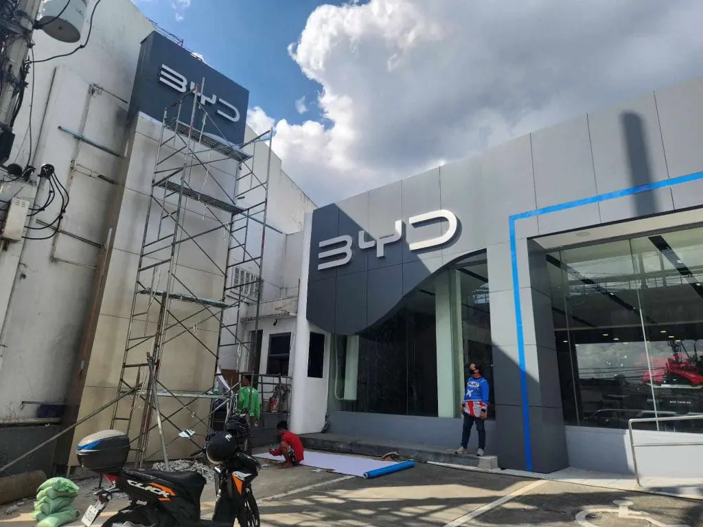 BYD metallic storefront acrylic signage installation in Mandaluyong with workers, scaffolding, and motorbikes by M&G Global Ads.