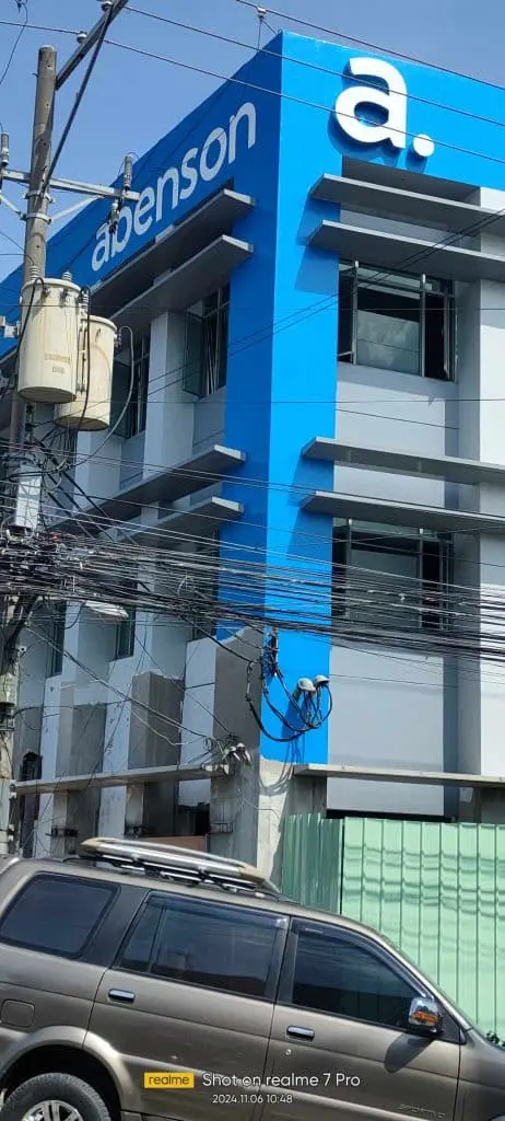 Abenson LED signage on a blue and white storefront in Quezon City, silver SUV parked in front, by M&G Global Ads.