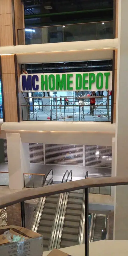 MC HOME DEPOT indoor metallic signage installation above escalator in Makati, with workers on-site by M&G Global Ads.