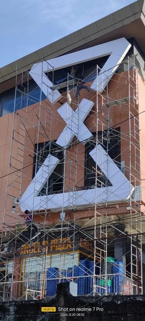Worker on scaffolding installs metallic building signage and clock structure in Mandaluyong, ongoing construction by M&G Global Ads.