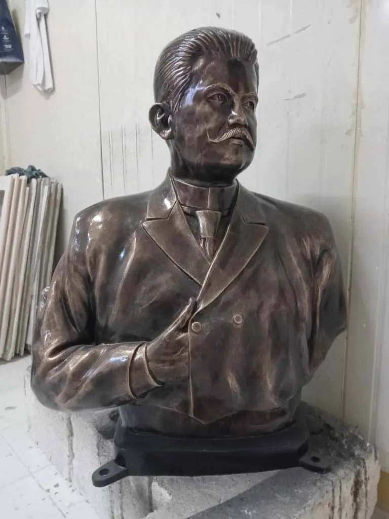 Bronze bust near corporate building signage in Quezon City, man with mustache and suit, indoors. By M&G Global Ads.