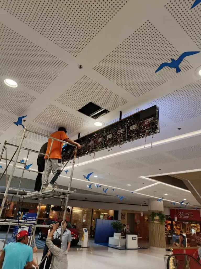 LED signage panel installation on shopping mall ceiling in Quezon City, blue bird decor and shops visible. By M&G Global Ads.