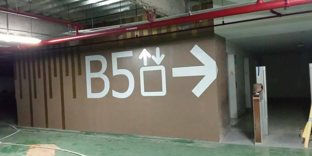 Elevator indoor signage in Makati parking garage with B5 text, arrows, and symbols on brown wall by M&G Global Ads.