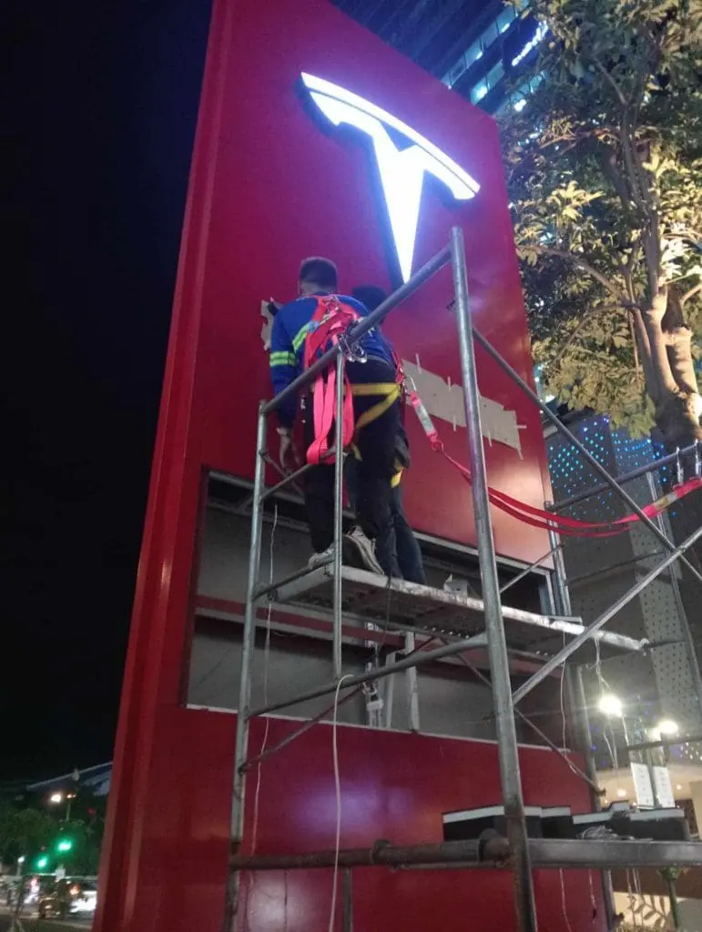 Workers installing large illuminated metal building sign on red structure at night in Makati by M&G Global Ads.