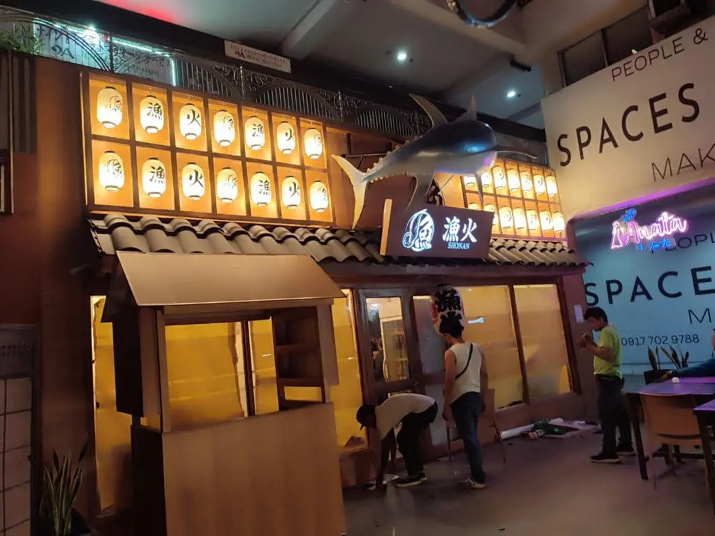 Japanese and English indoor signage at shark-themed restaurant in Makati, glowing lanterns, wood stall outside by M&G Global Ads.