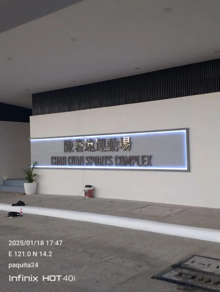 Outdoor building signage for CHAN CHAN SPORTS COMPLEX on a white wall in Ortigas by M&G Global Ads. Tools and paint can nearby.