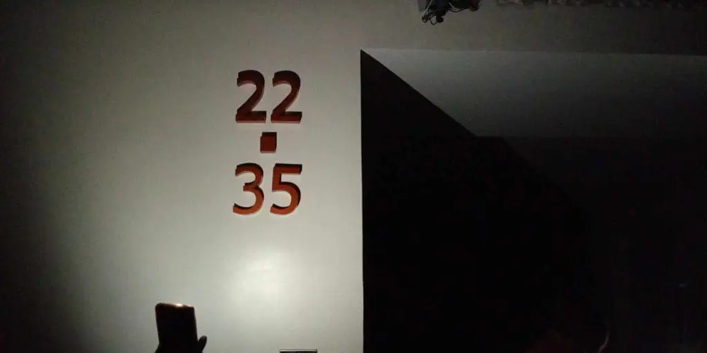 22/35 acrylic signage displayed on a dim wall, phone glowing in foreground, Makati installation by M&G Global Ads.