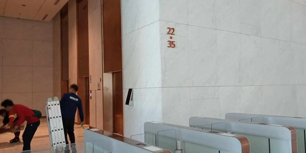 Acrylic signage installation near elevators in modern Makati lobby with marble walls, floor indicators, by M&G Global Ads.