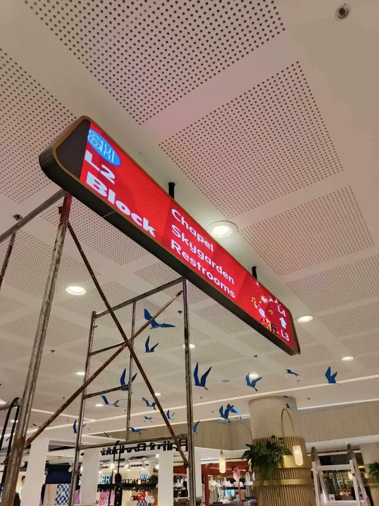 Mall directional signage for restrooms, chapel, and sky garden in Makati, red metallic finish. Scaffolding below. by M&G Global Ads.