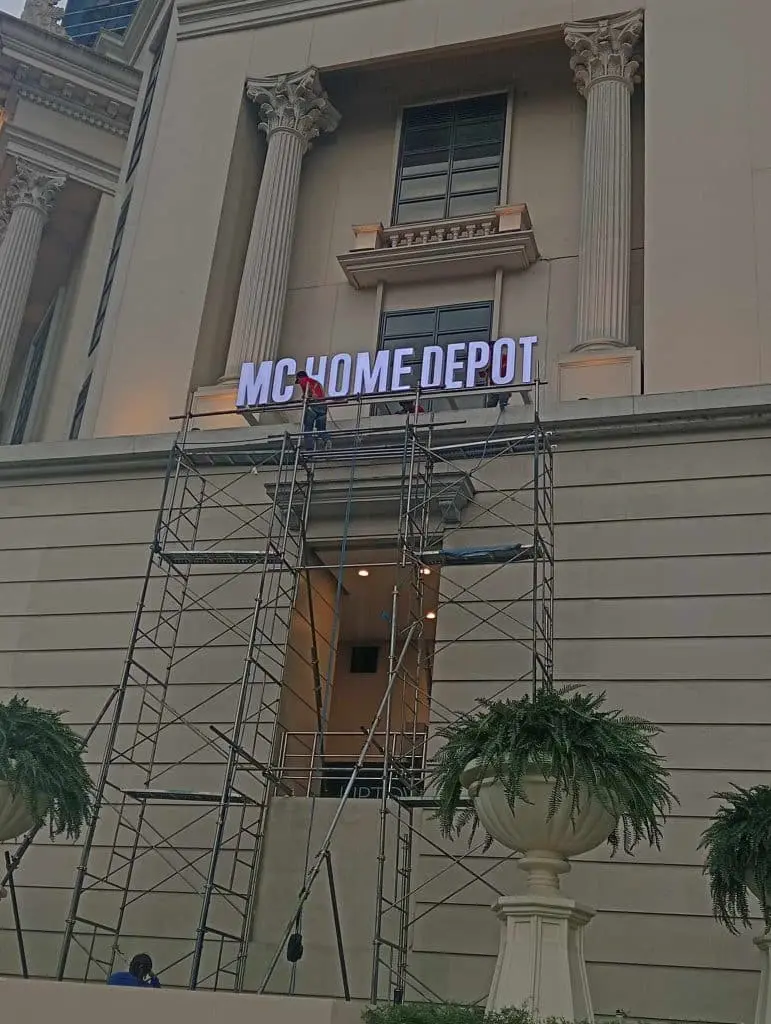 Metallic building signage installation for MC HOME DEPOT in Quezon City by M&G Global Ads, workers on scaffolding visible.