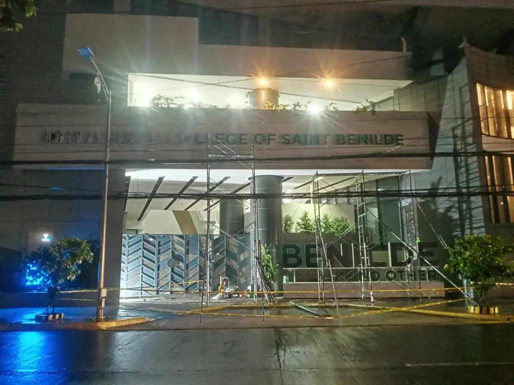 Illuminated De La Salle College of Saint Benilde outdoor signage in Makati, partly covered by scaffolding, by M&G Global Ads.