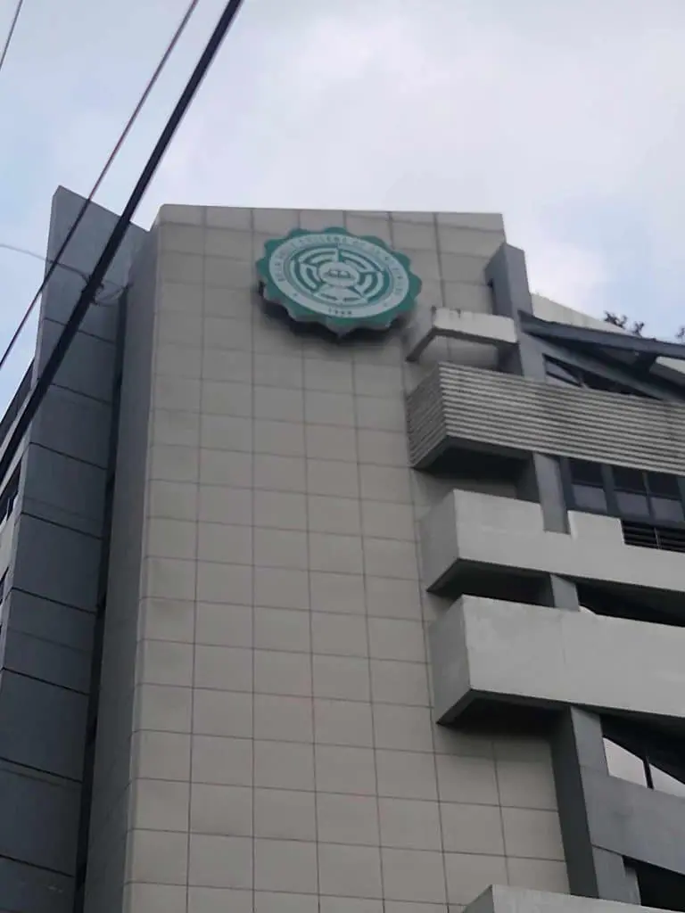 Metallic building signage with teal and white gear emblem in Quezon City, cloudy sky, power lines—by M&G Global Ads.