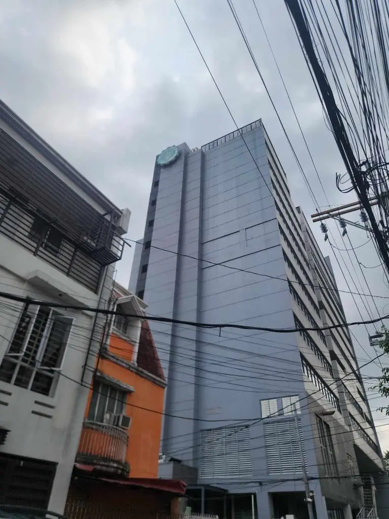 Light blue modern building with outdoor billboard signage in Makati, among older structures and wires, by M&G Global Ads.