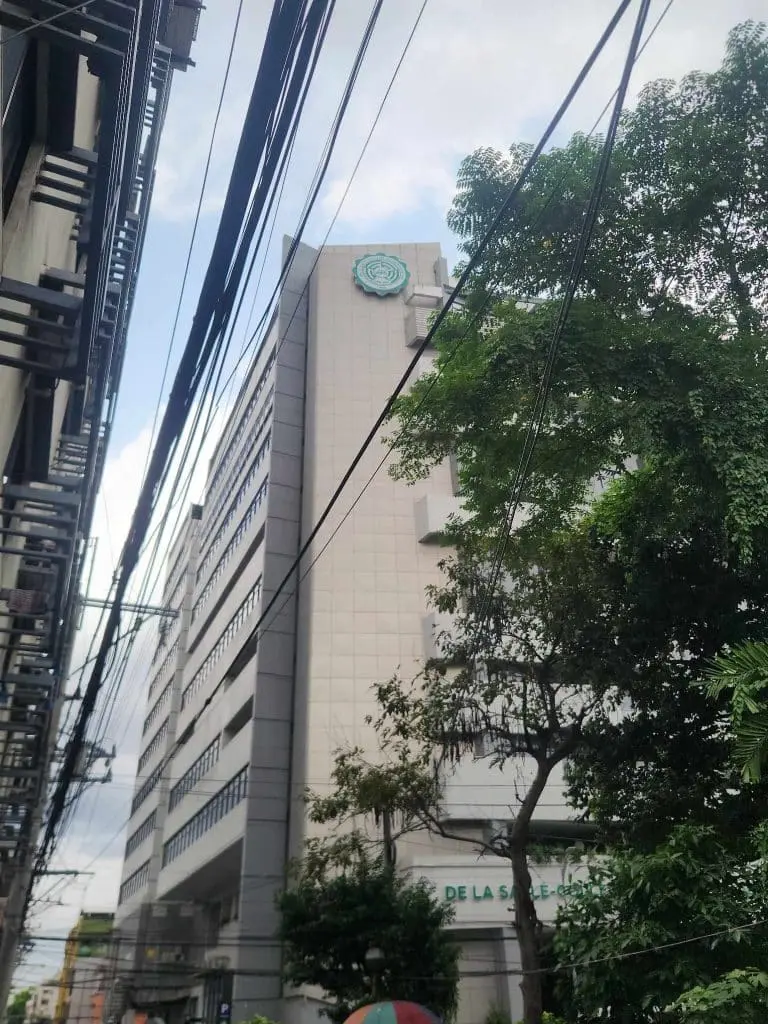 De La Salle University outdoor building signage in Makati, with street view, trees, and power lines. By M&G Global Ads.