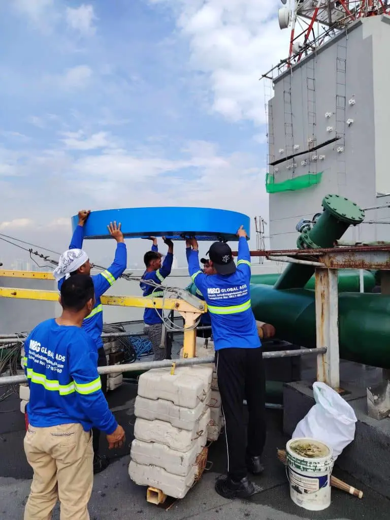 Workers install a large round metal billboard sign on a Makati rooftop with tools and equipment by M&G Global Ads.