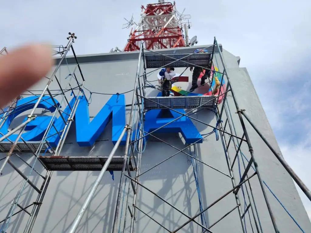 GMA outdoor building signage installation in Quezon City with rainbow heart logo, workers on scaffolding by M&G Global Ads.