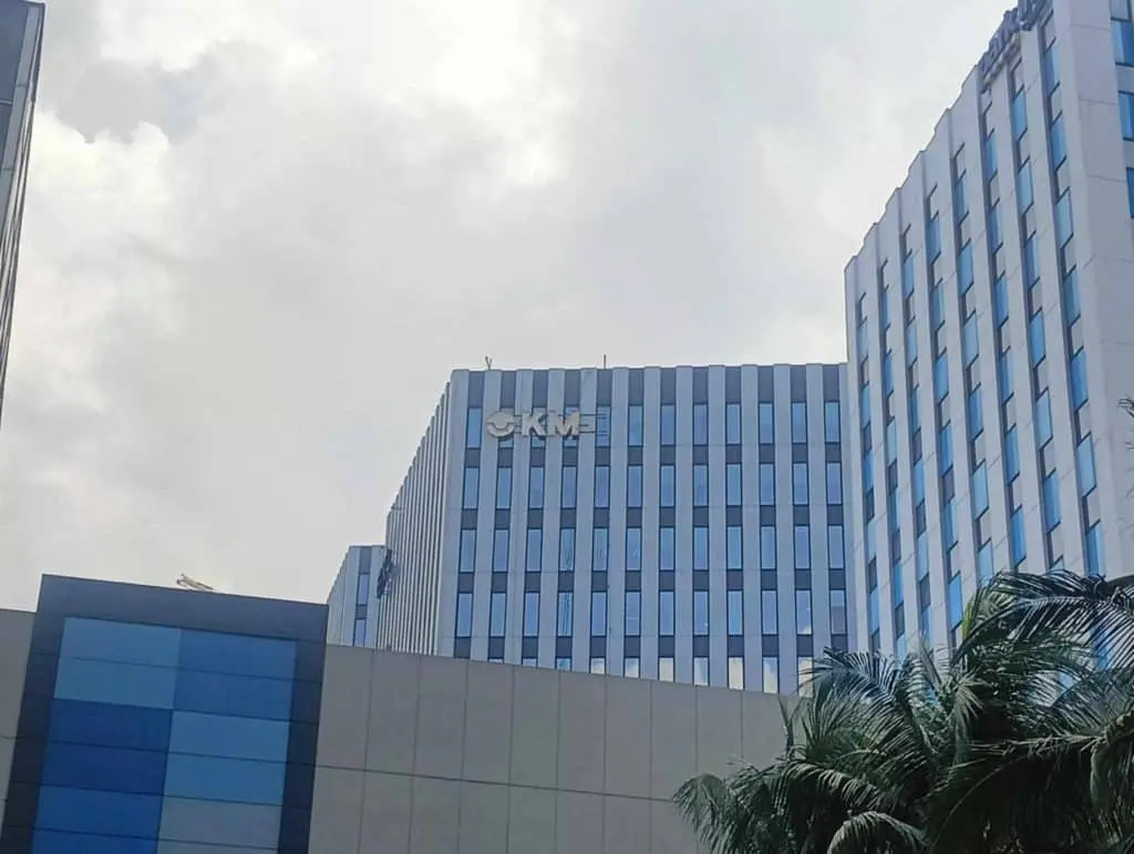 Office building with blue-tinted windows and pylon signage in Makati, cloudy sky, palm trees—by M&G Global Ads.