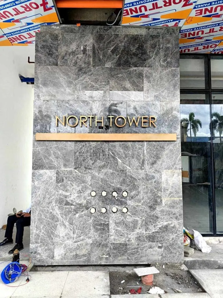 Lobby signage for NORTH TOWER in gold letters, marble wall, lights, Makati construction site by M&G Global Ads.