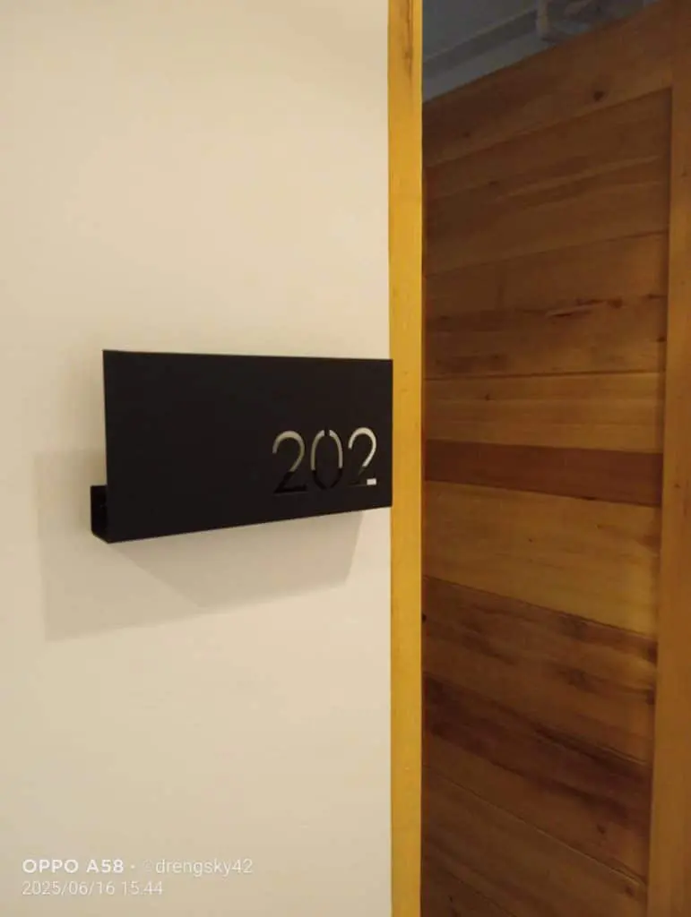 Acrylic room signage 202 black cut-out on white wall by wooden door in Quezon City, by M&G Global Ads.