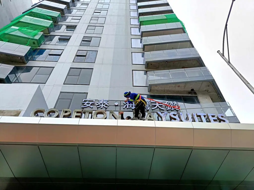 Hotel building signage installation for Copelton baysuites in Aseana Pasay by M&G Global Ads. Worker on high-rise with harness and helmet.