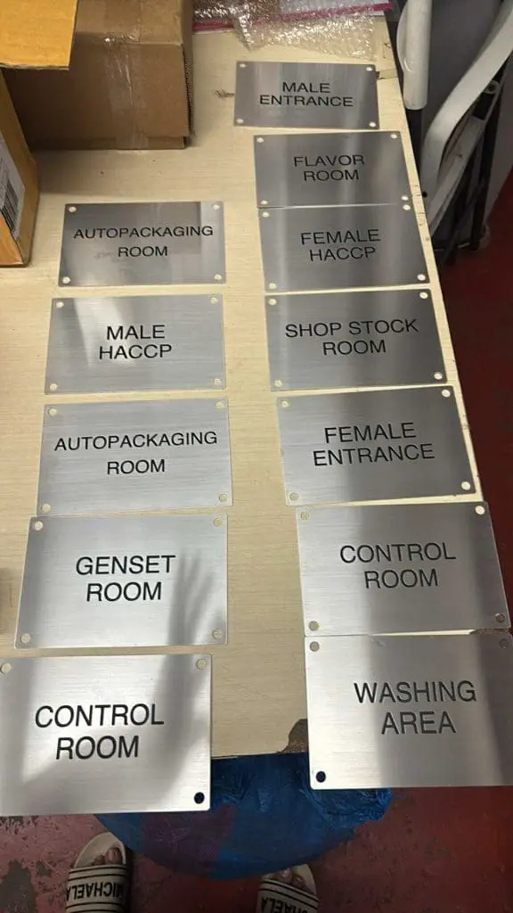 stainless engrave door signs CONTROL ROOM, MALE ENTRANCE, etc., displayed on wood in Ortigas by M&G Global Ads. Persons feet partly shown.