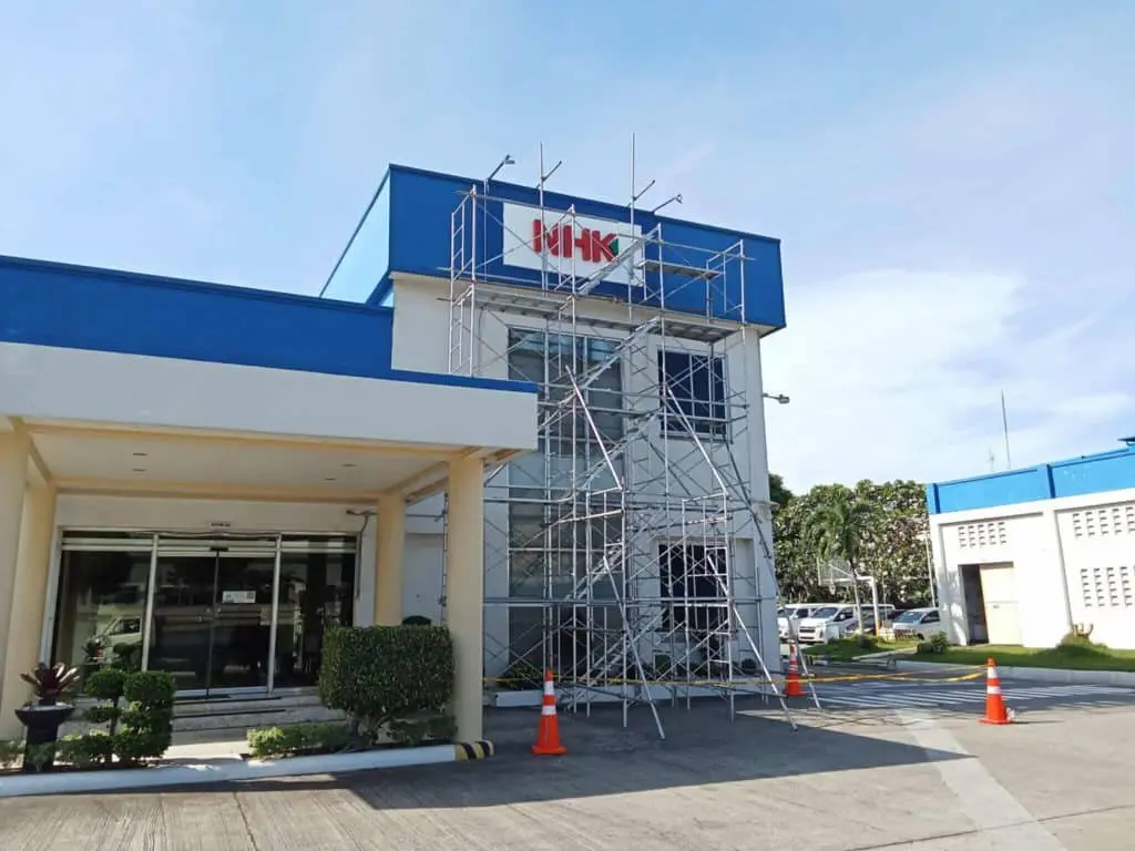 MHK acrylic building signage under construction with scaffolding and cones in Makati, clear sky, by M&G Global Ads.